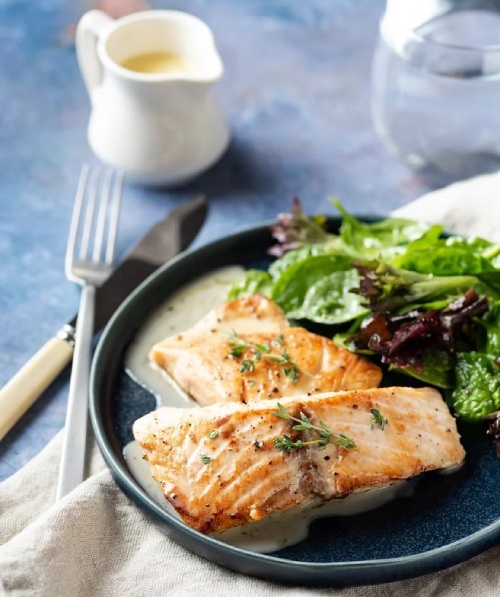 Cooked salmon on black plate with a side salad.